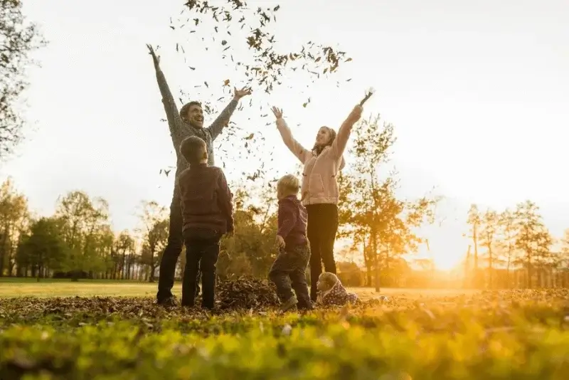 a family throwing leaves in the air at sunset