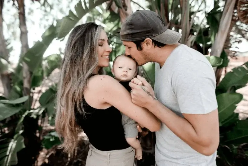 A couple holding a baby in front of palm trees